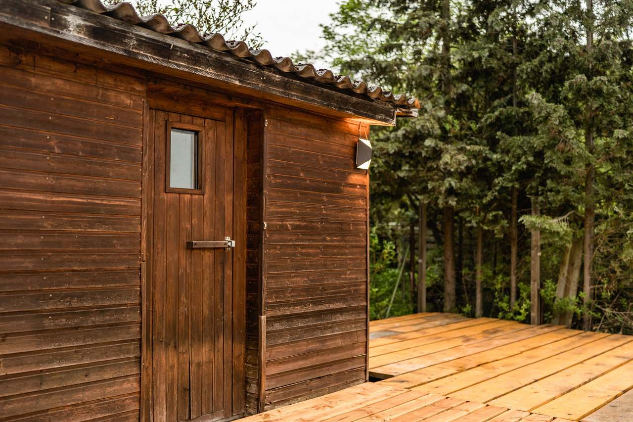 Holzhütte mit Tür und Holzterrasse vor hohen Nadelbäumen