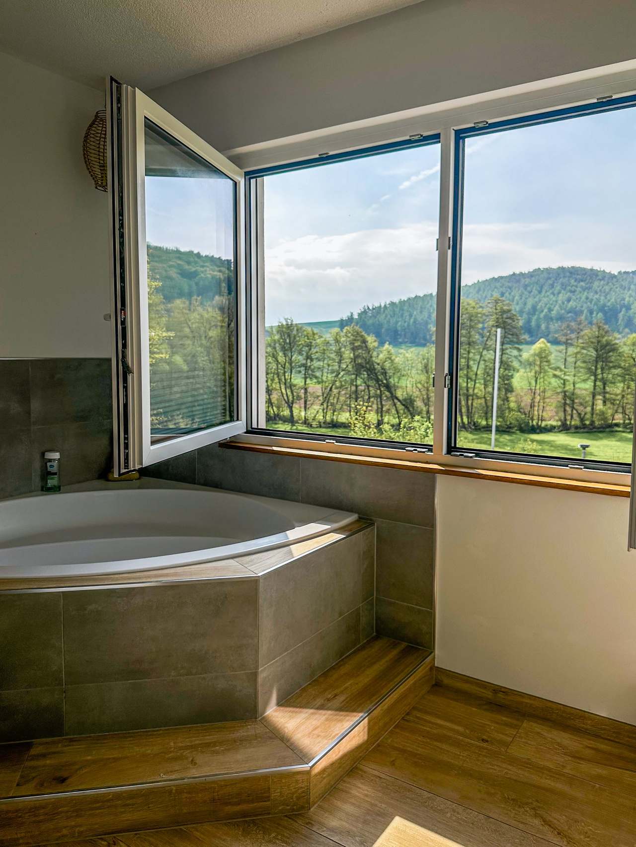 Badezimmer mit Eckbadewanne und großem Fenster mit Blick ins Grüne