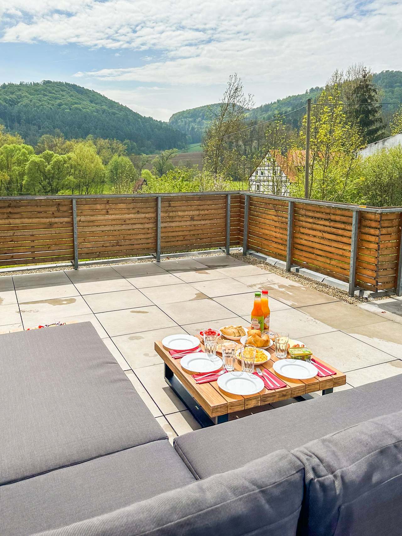 Große Dachterrasse mit Loungesofa, gedecktem Tisch und Blick auf Hügel