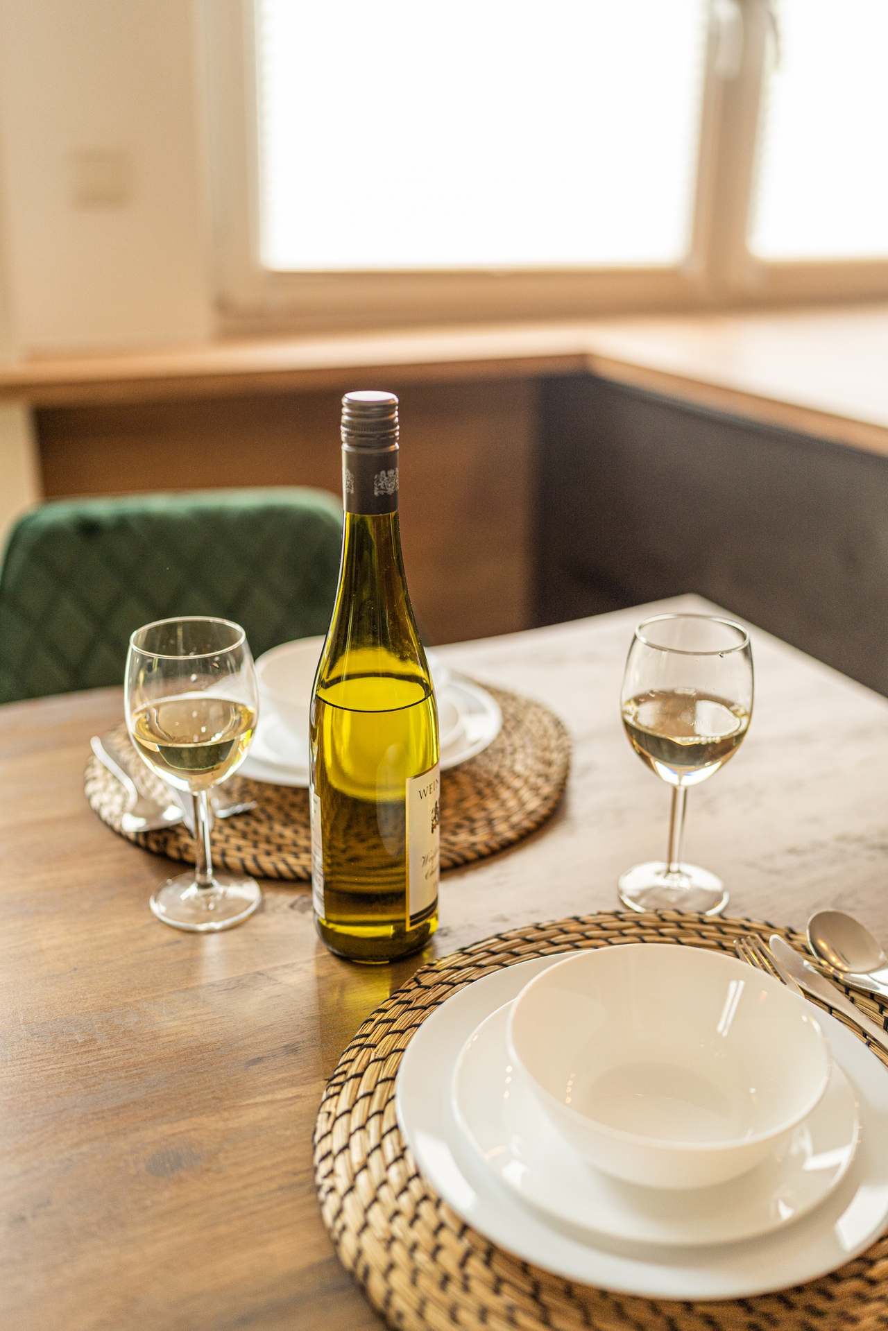Gedeckter Esstisch mit Weißwein, zwei Gläsern und weißem Geschirr