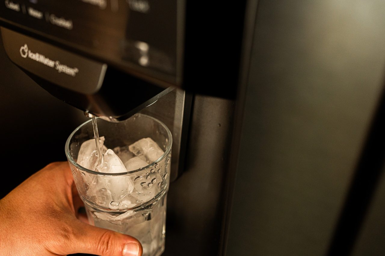Hand füllt ein Glas mit Eis am Kühlschrankspender