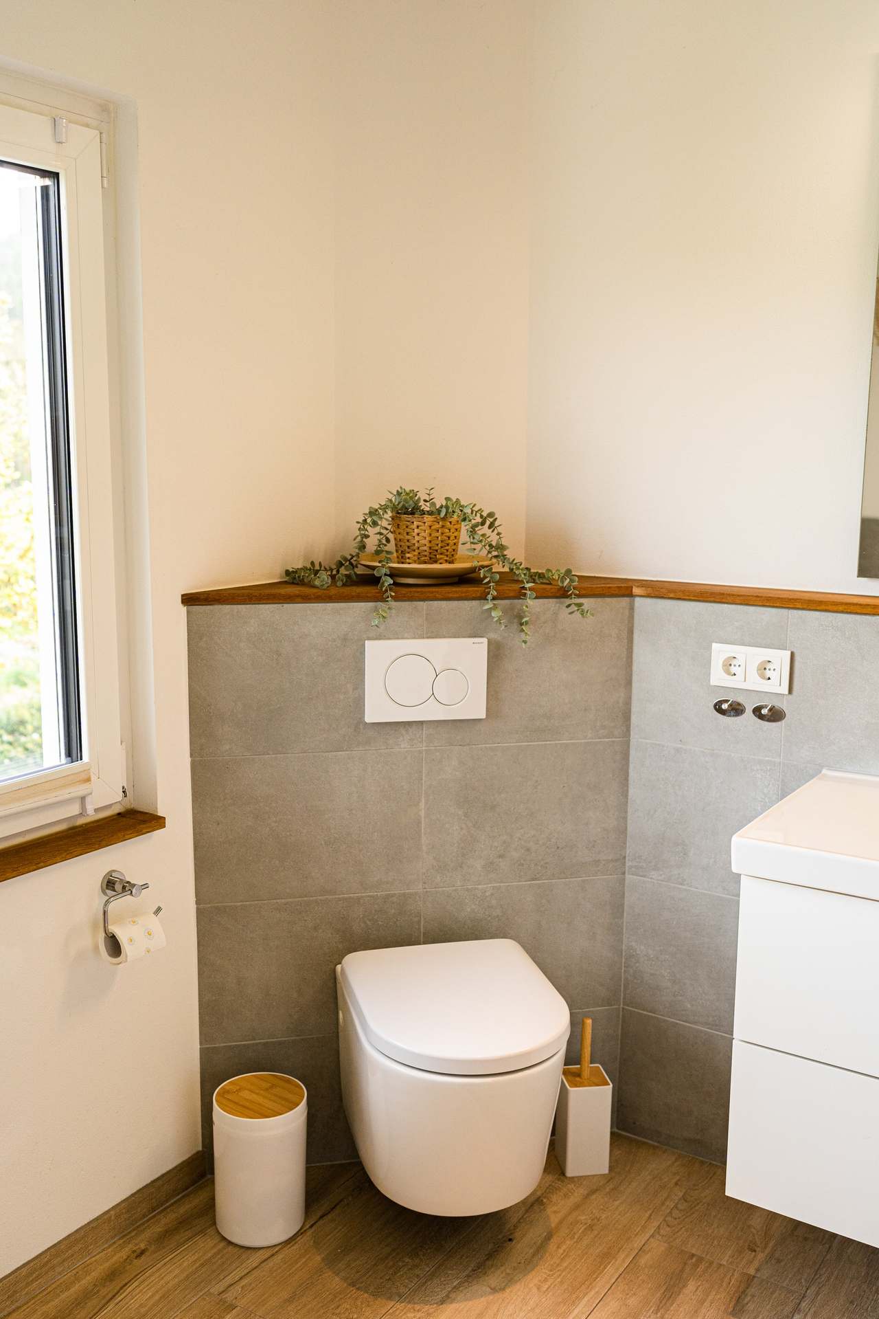 Badezimmer mit Wand-WC, grauen Fliesen und Pflanze auf der Ablage