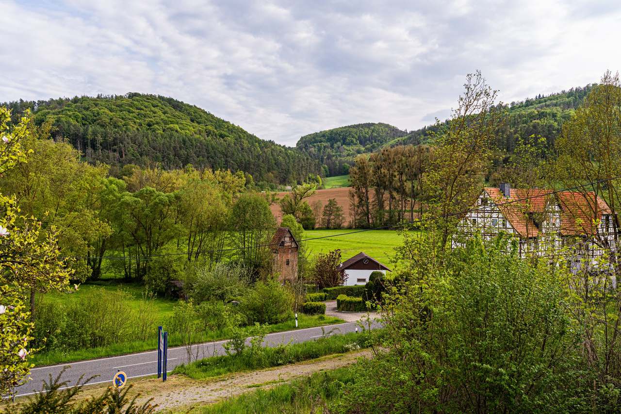 Blick auf grüne Hügel, Wiesen und Fachwerkhäuser an einer Straße
