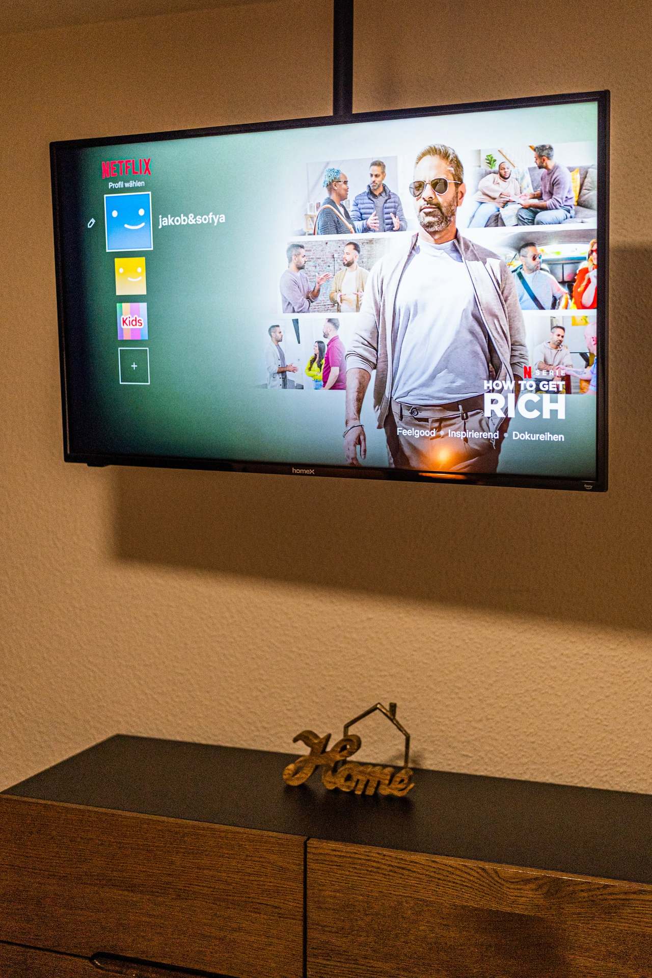 Wandfernseher über einer dunklen Kommode mit Home-Schriftzug
