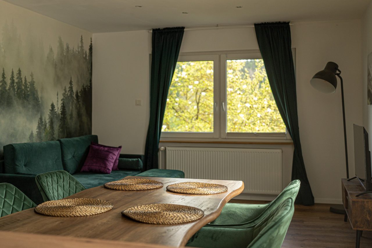 Wohn- und Essbereich mit grünem Sofa, Holztisch und großem Fenster
