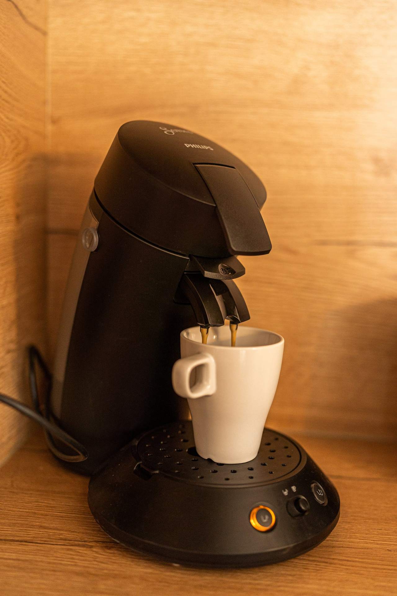 Kaffeepadmaschine mit weißer Tasse auf Holzarbeitsplatte