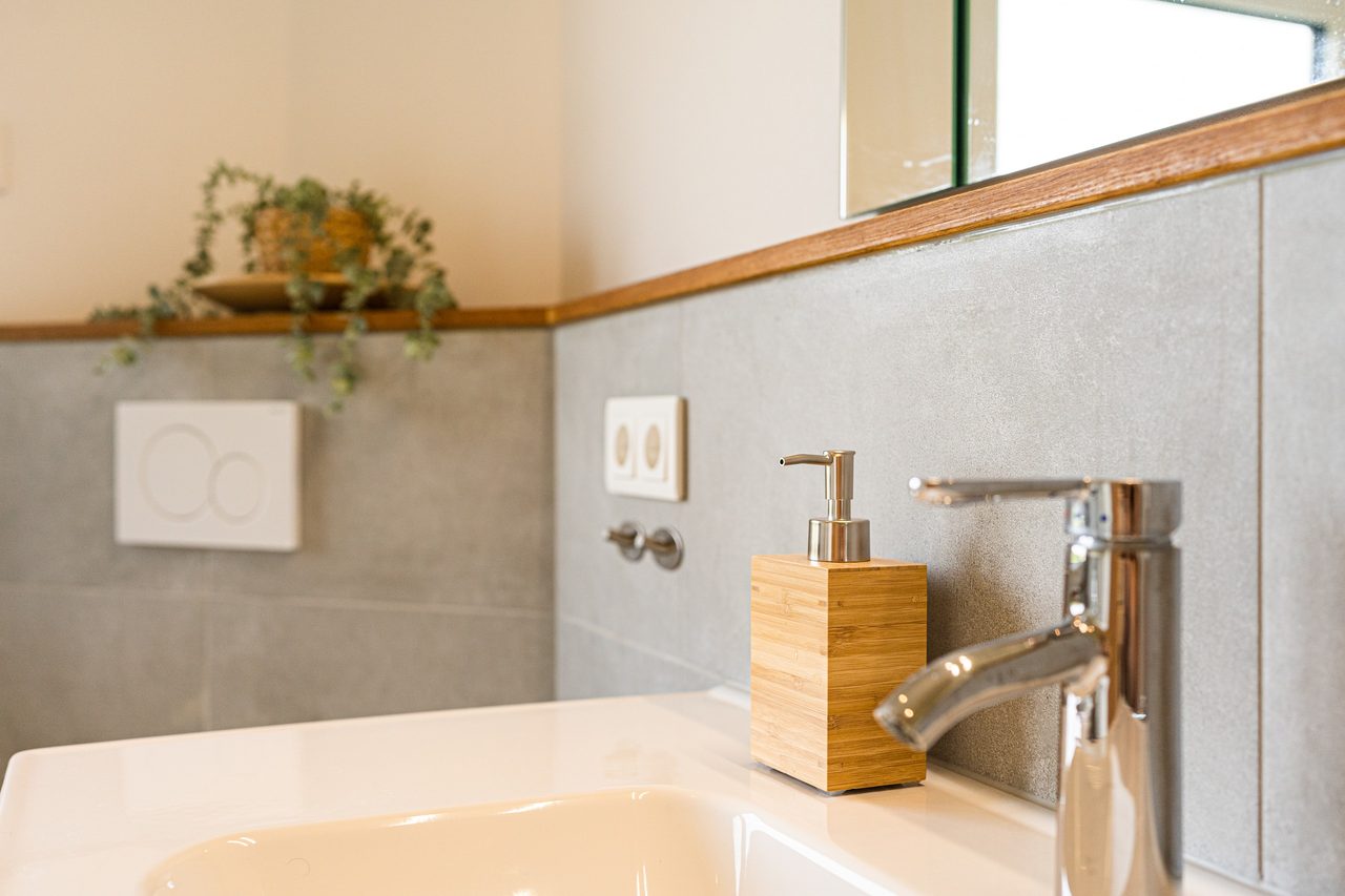 Badezimmer mit Waschbecken, Chromarmatur und Seifenspender aus Holz