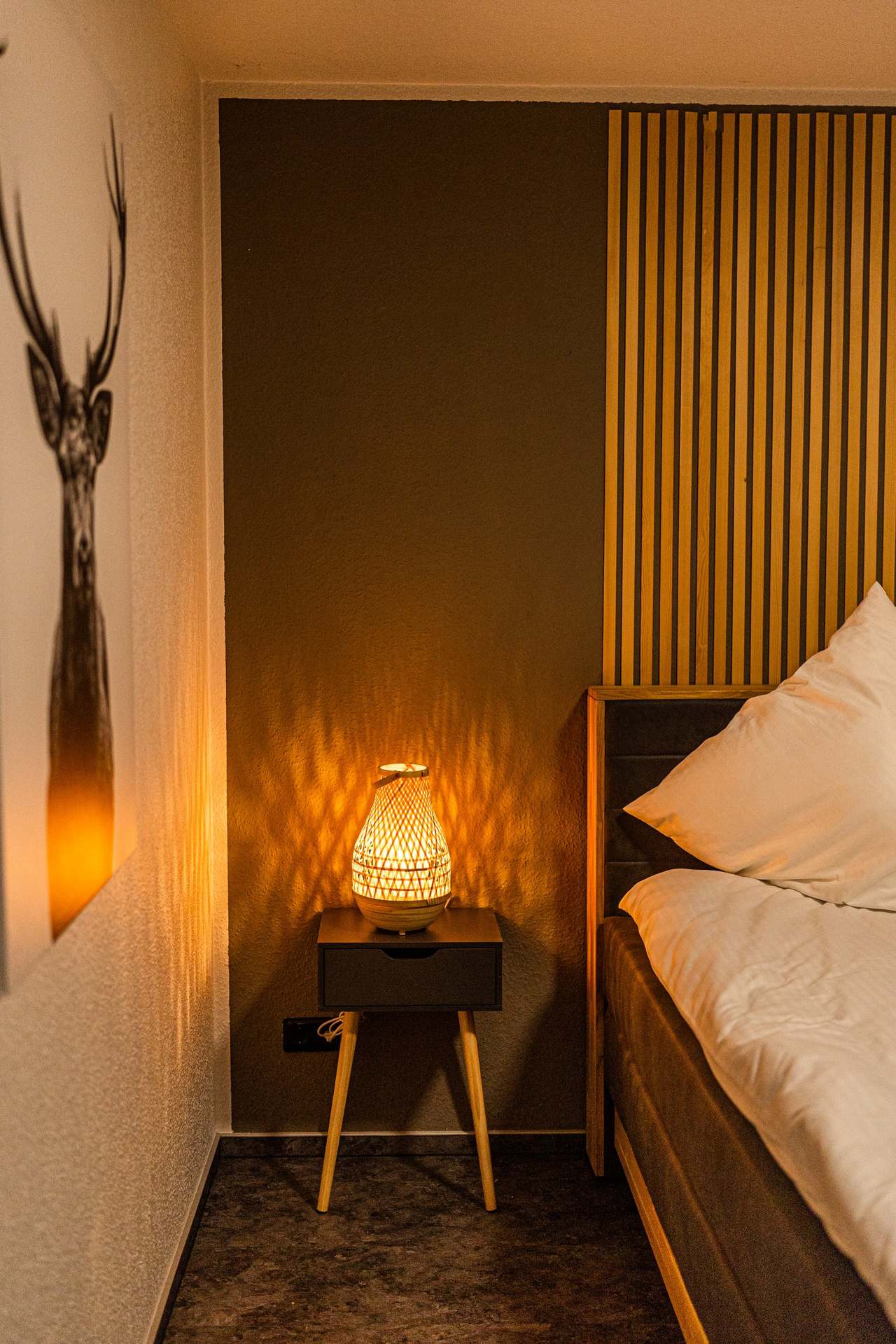 Schmales Schlafzimmer mit Bett, Hirschbild und Nachttischlampe