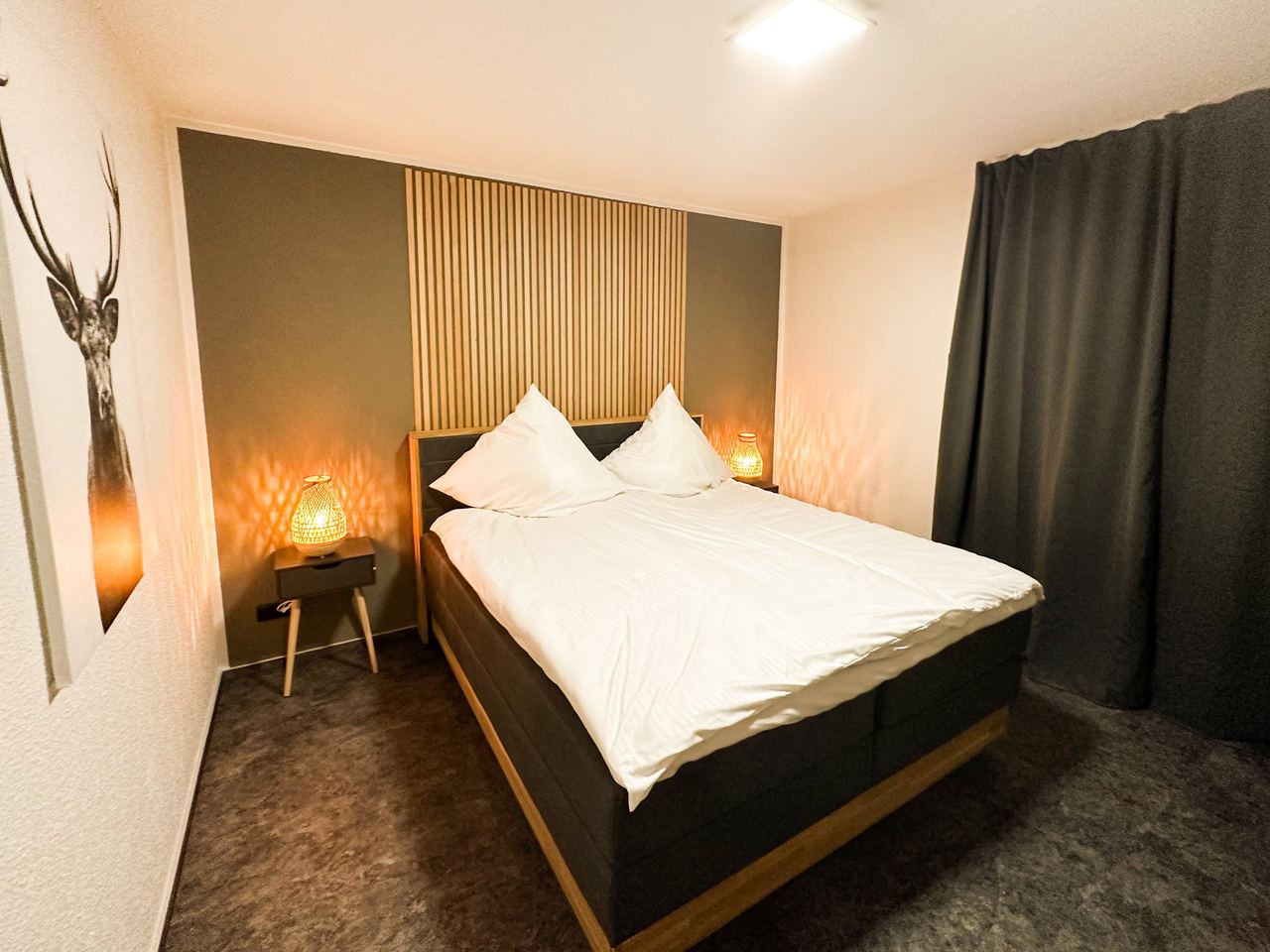 Schlafzimmer mit Doppelbett, Holzlamellenwand und dunklem Vorhang
