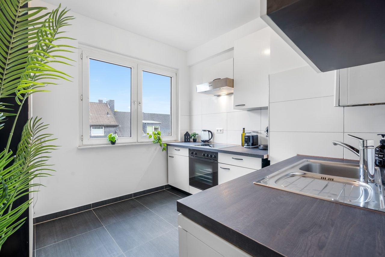 Küche mit weißen Schränken, Spüle und Fenster