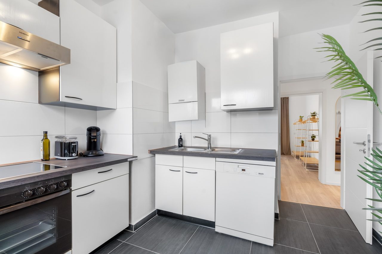 Küche mit weißen Schränken, Backofen und Blick in den Flur