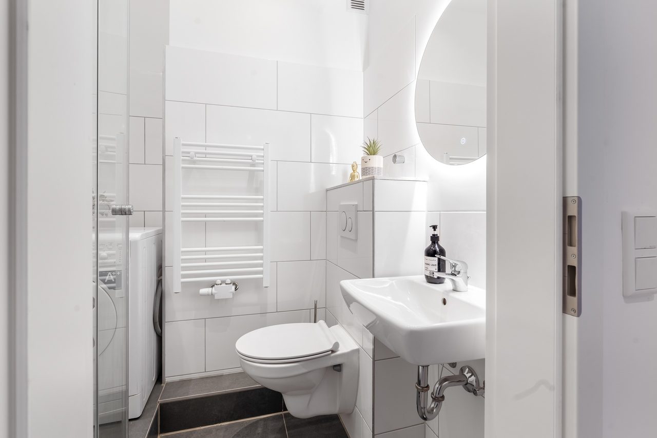 Badezimmer mit Wand-WC, Waschbecken und rundem Spiegel