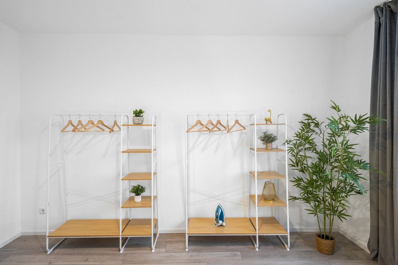 Zwei weiße Kleiderregale mit Holzbügeln und Bambuspflanze