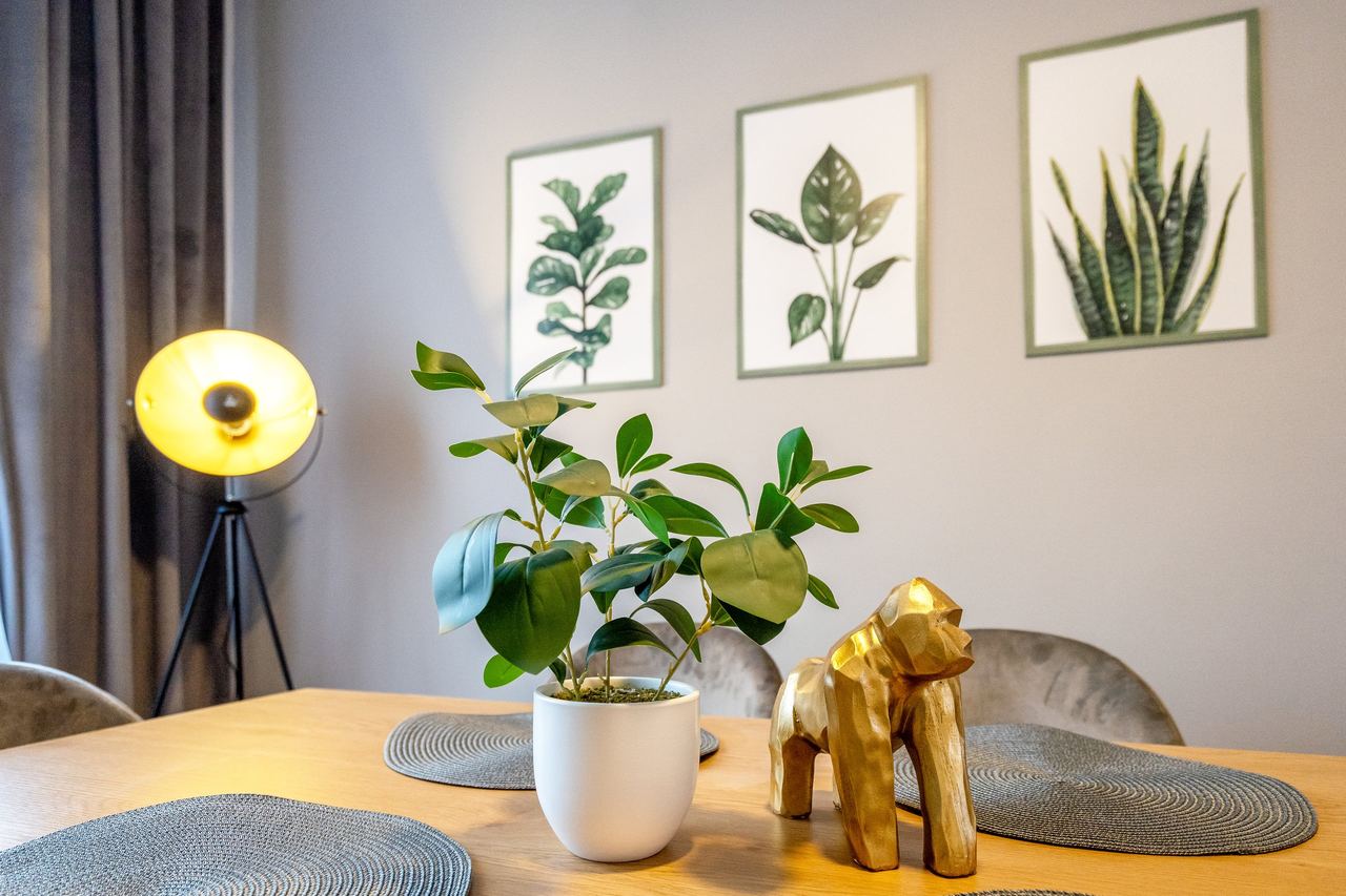 Esstisch mit Topfpflanze, goldener Figur und Pflanzenbildern