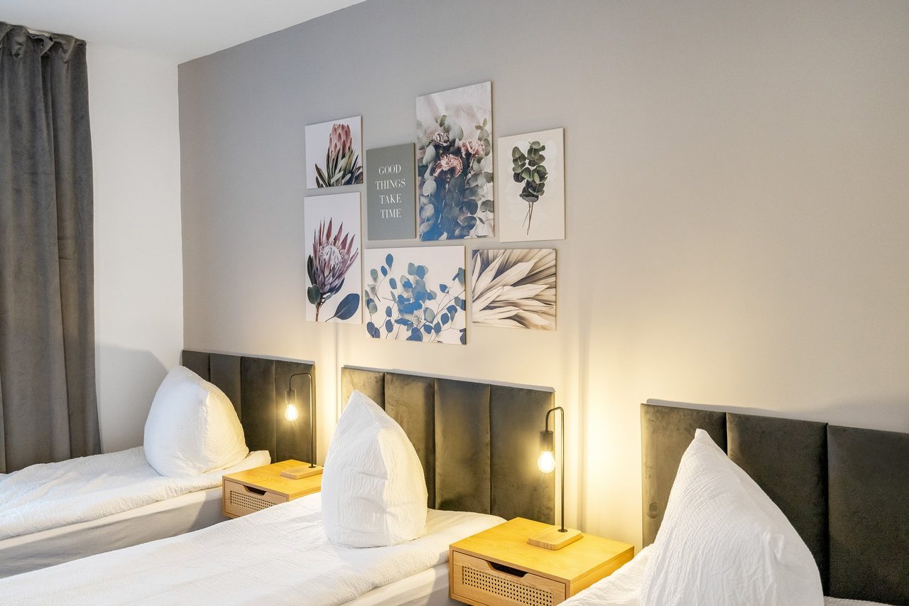 Schlafzimmer mit Einzelbetten, Nachttischen mit Lampen und Bilderwand