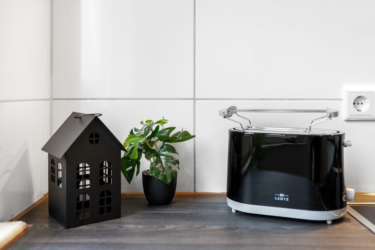 Schwarzer Toaster, Topfpflanze und Deko Haus auf Arbeitsplatte