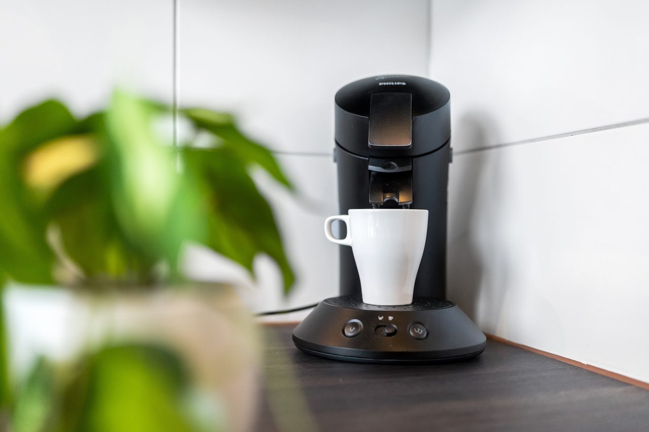 Kaffeepadmaschine mit weißer Tasse auf dunkler Arbeitsplatte
