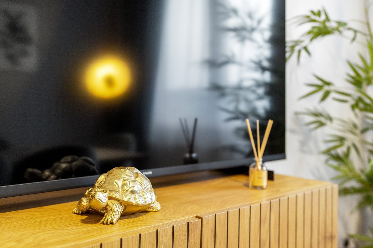 Fernseher auf Holzsideboard mit goldener Schildkröte und Duftstäbchen