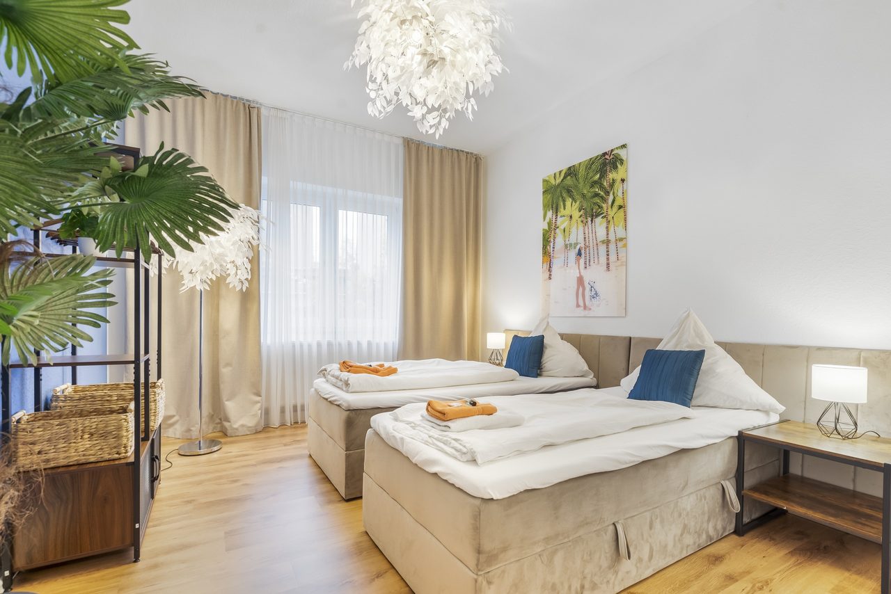 Schlafzimmer mit zwei Einzelbetten, orangen Handtüchern und Palmenbild