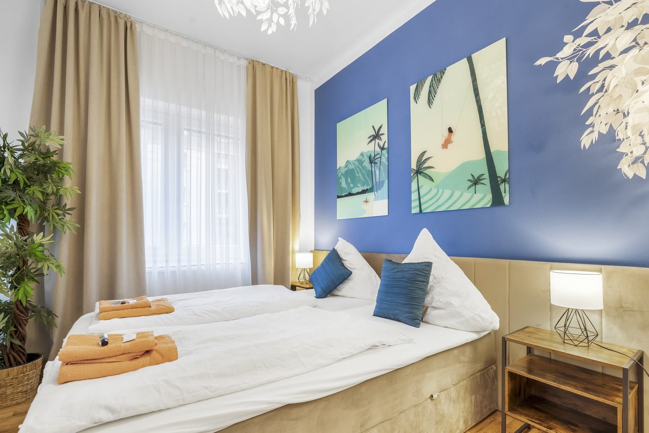 Schlafzimmer mit blauer Wand, Palmenbildern und Doppelbett mit blauen Kissen
