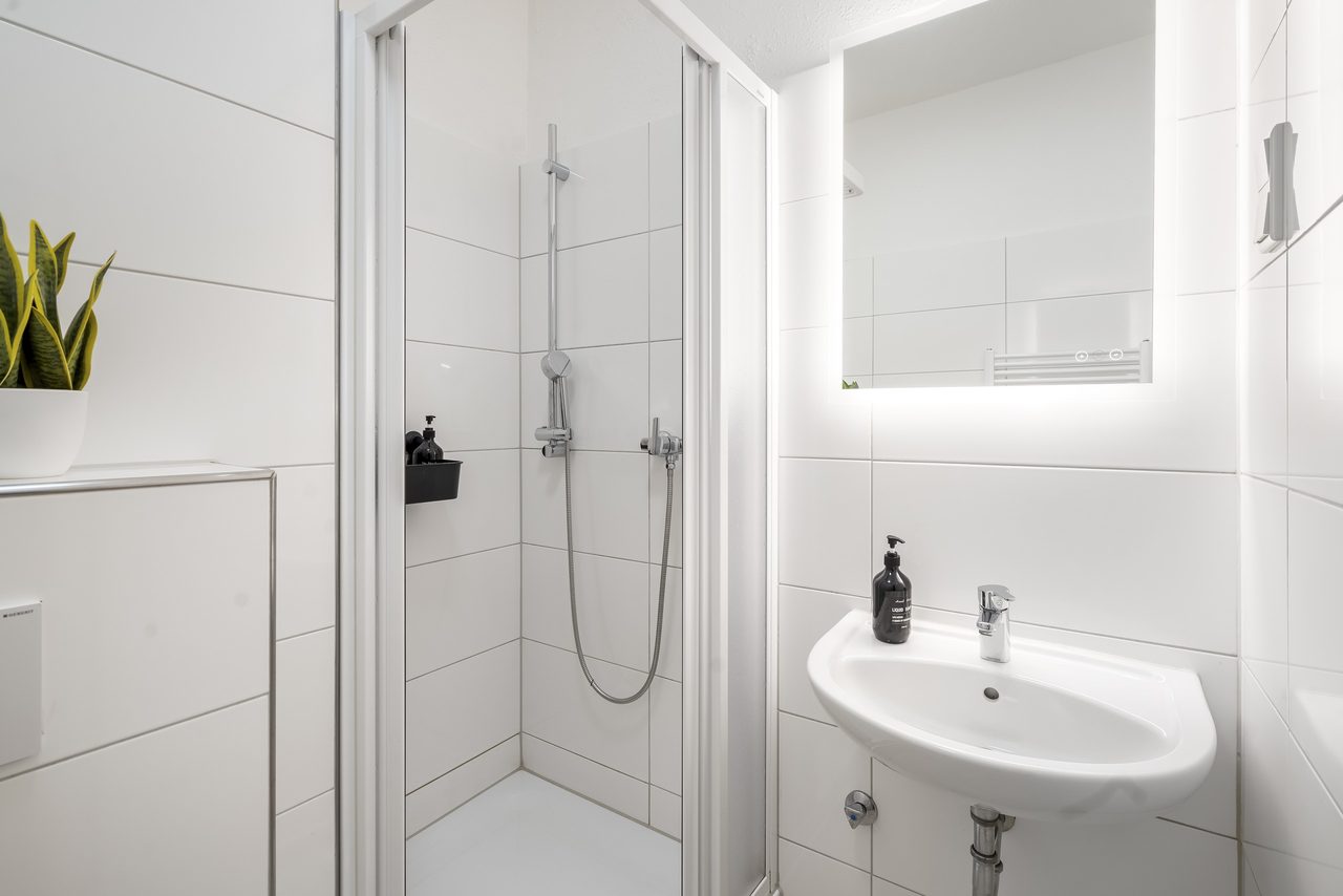 Duschbad mit Glasdusche, Waschbecken und beleuchtetem Spiegel