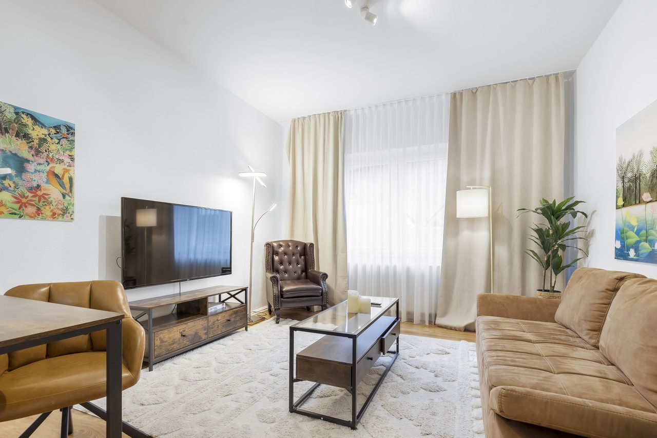 Wohnzimmer mit Fernseher, Ohrensessel aus Leder und braunem Sofa