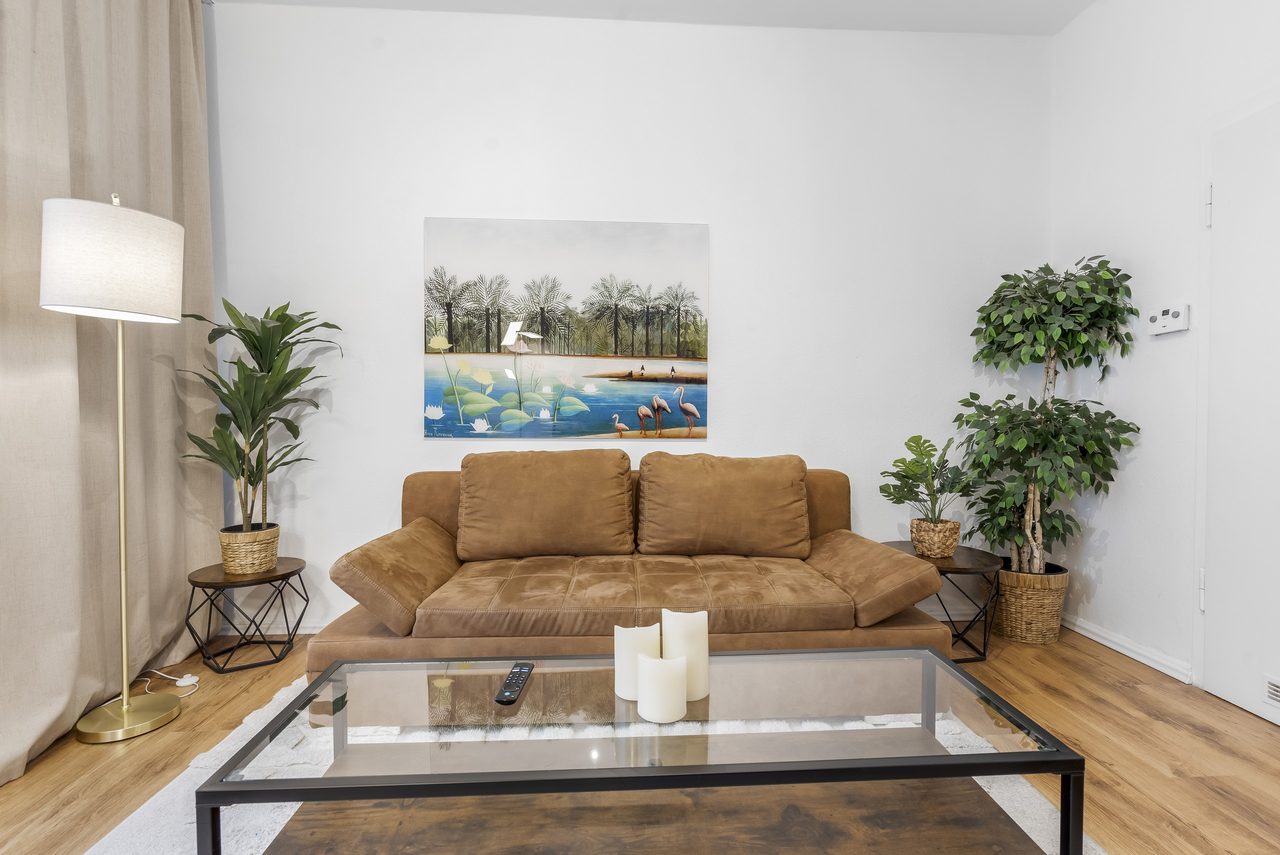 Wohnzimmer mit braunem Sofa, Glascouchtisch und Stehlampe