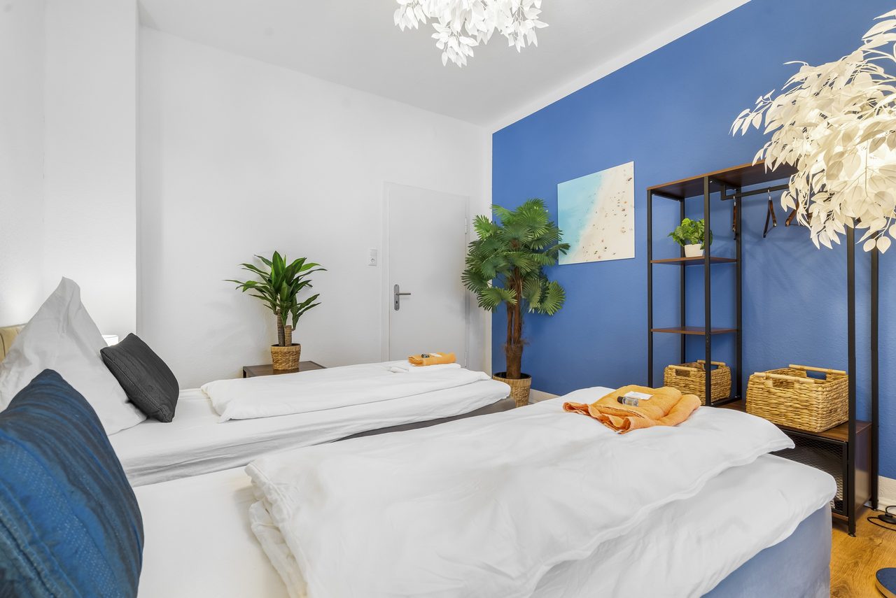 Schlafzimmer mit zwei Betten, blauer Wand und Metallregal