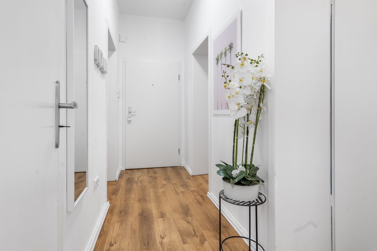 Flur mit Holzboden, weißen Türen und Orchidee auf einem Ständer