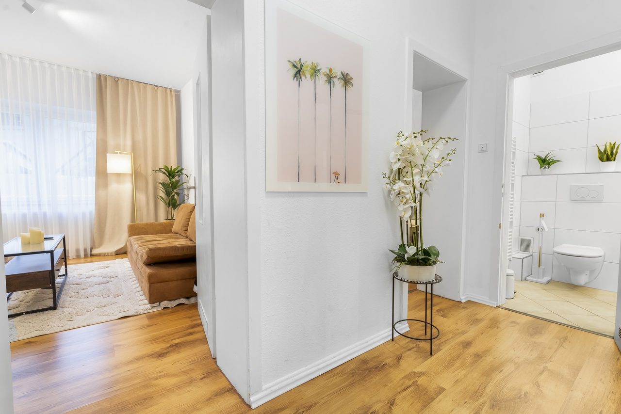 Flur mit Orchidee, Blick ins Wohnzimmer mit Sofa und ins Bad