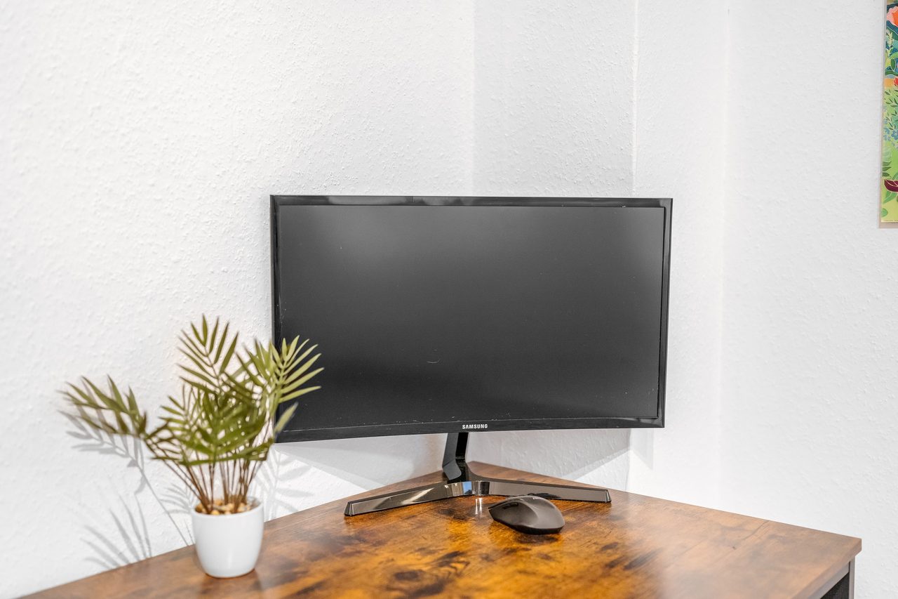 Schreibtisch aus Holz mit Monitor und kleiner Topfpflanze