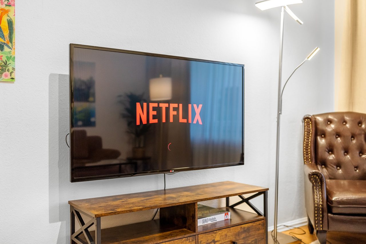 Wandfernseher über Holzlowboard, daneben Stehlampe und Ledersessel
