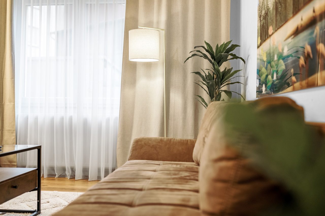 Wohnzimmer mit Sofa, Stehlampe und Vorhängen vor dem Fenster