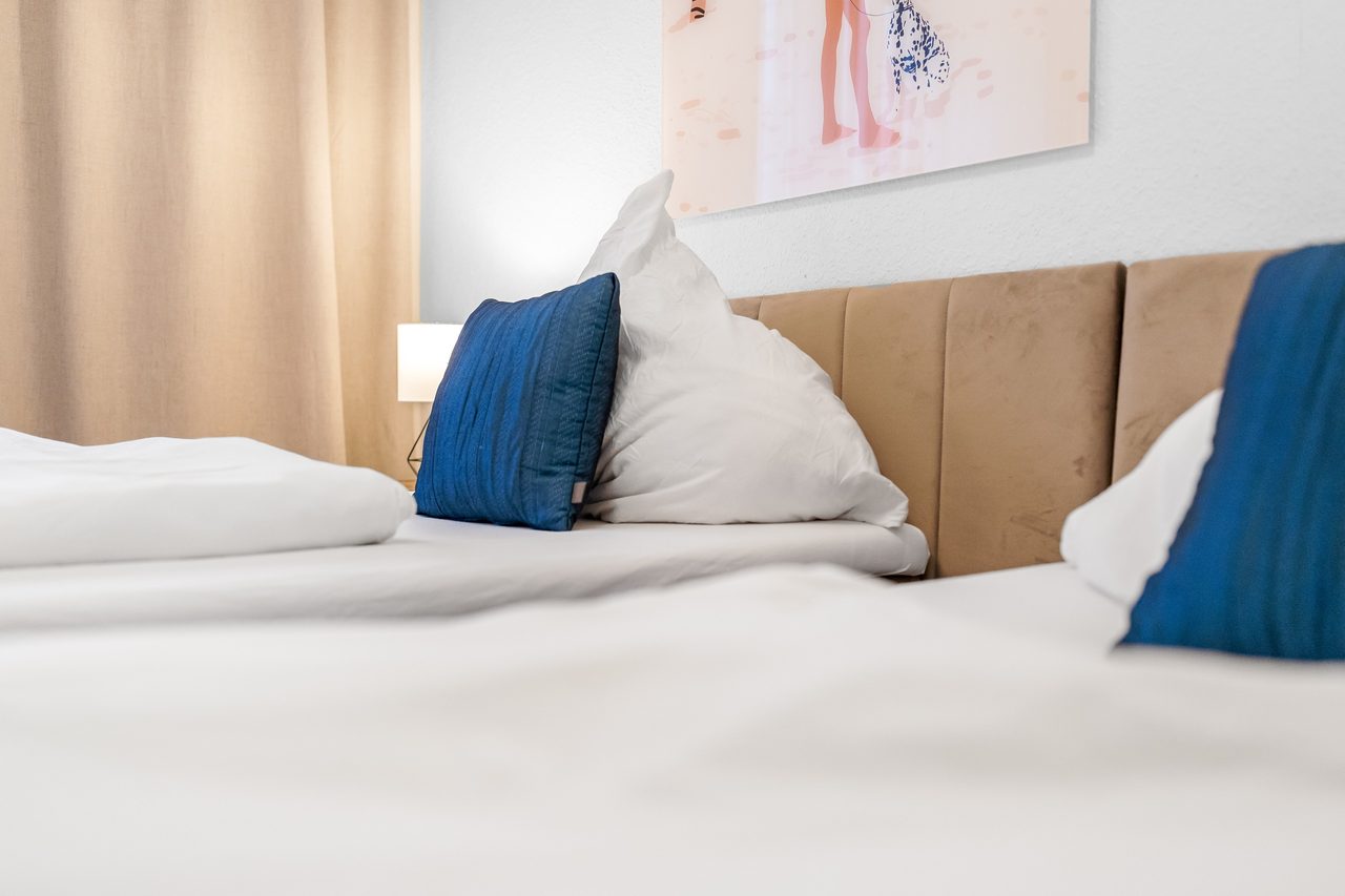 Bett mit weißer Bettwäsche, blauem Kissen und gepolstertem Kopfteil