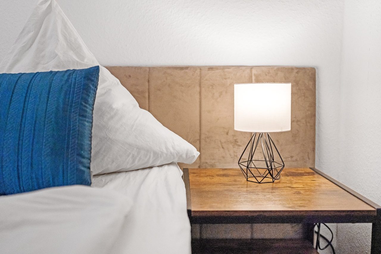 Bett mit blauem Kissen neben Nachttisch mit Lampe