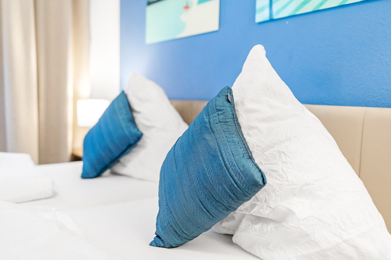 Bett mit weißen Kopfkissen und blauen Zierkissen