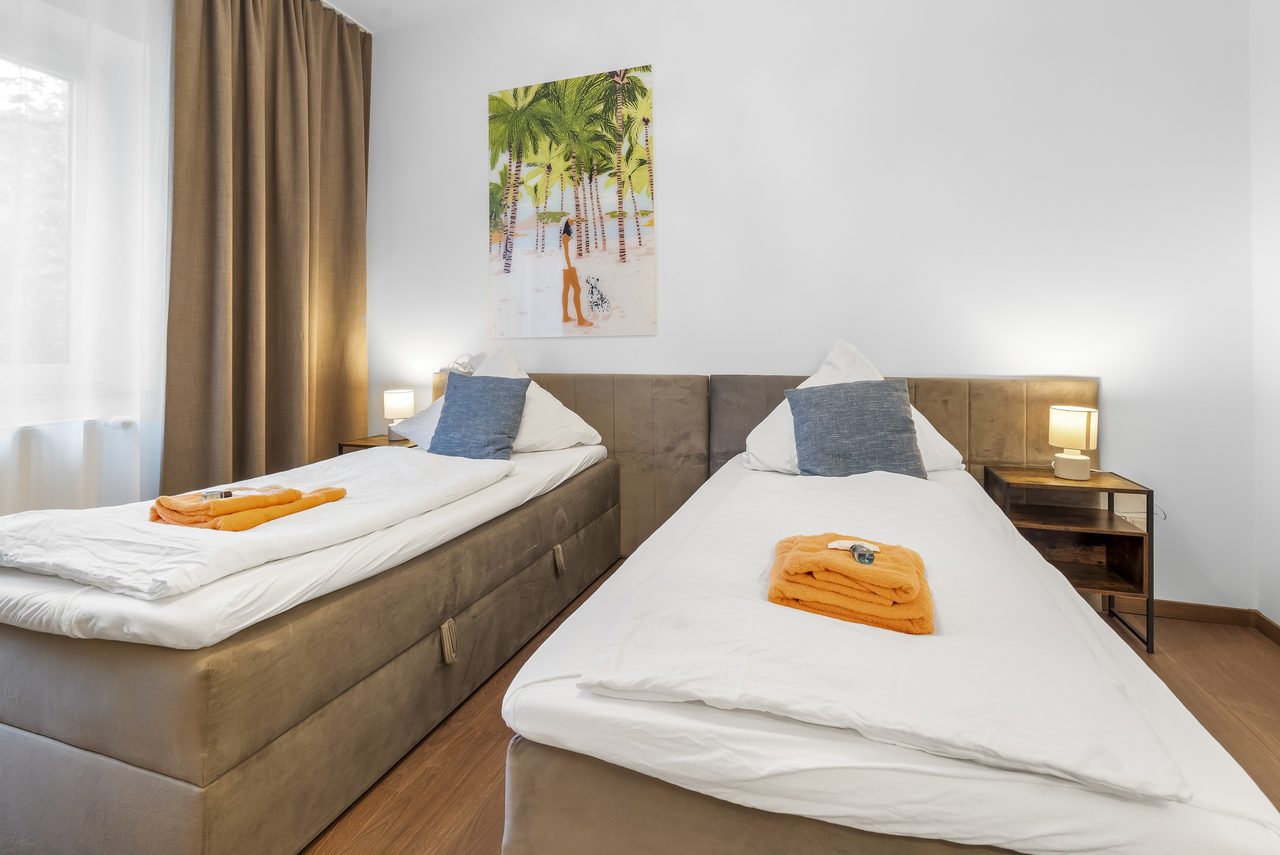 Schlafzimmer mit zwei Einzelbetten, orangen Handtüchern und Palmenbild