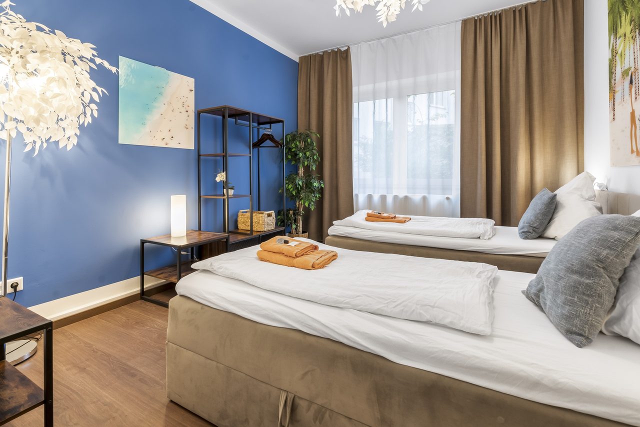 Schlafzimmer mit zwei Einzelbetten, blauer Wand und Metallregal