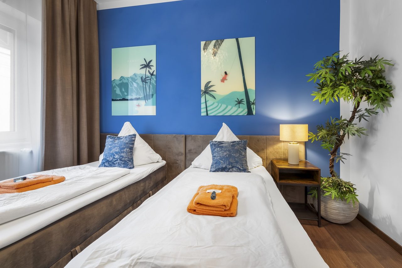 Schlafzimmer mit zwei Einzelbetten, blauer Wand und Palmenbildern