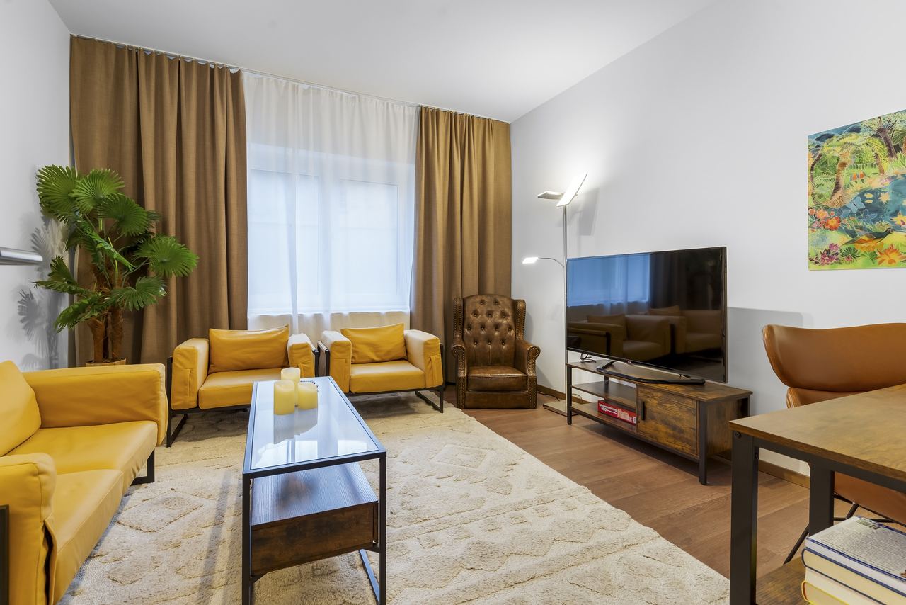 Wohnzimmer mit gelben Sesseln, Fernseher und Glascouchtisch