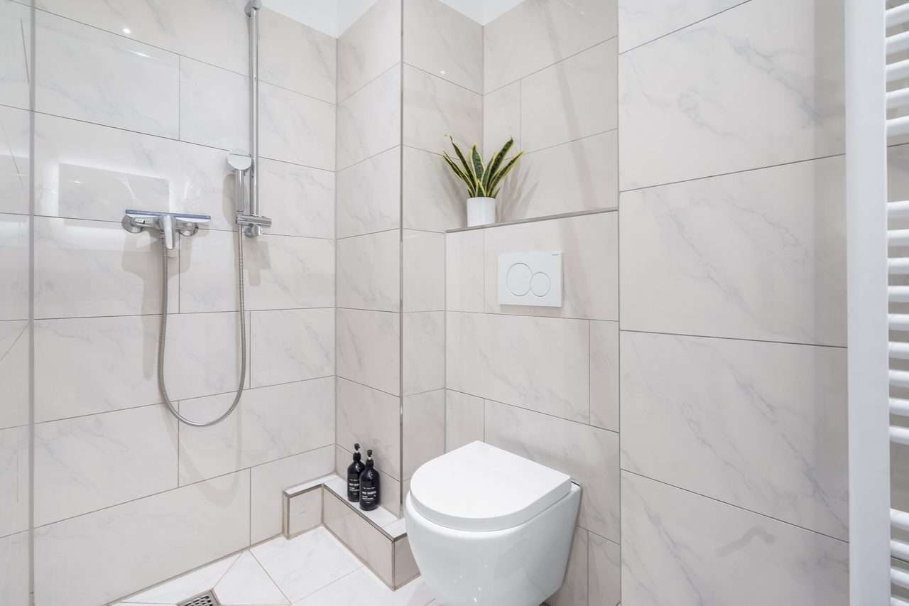 Duschbad mit Glasdusche, Wand-WC und grauen Fliesen