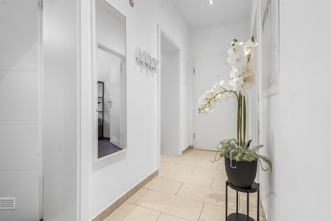 Flur mit Fliesenboden, Wandspiegel und Orchidee auf einem Ständer