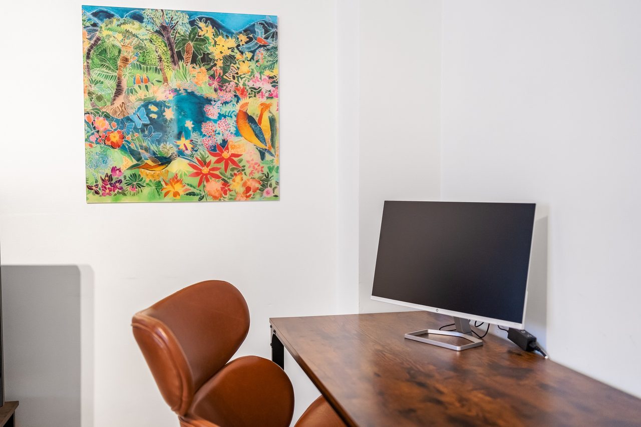 Schreibtisch mit Monitor, braunem Stuhl und buntem Wandbild