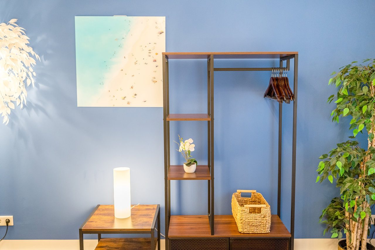 Blaue Wand mit Strandbild, Kleiderregal und Tischlampe