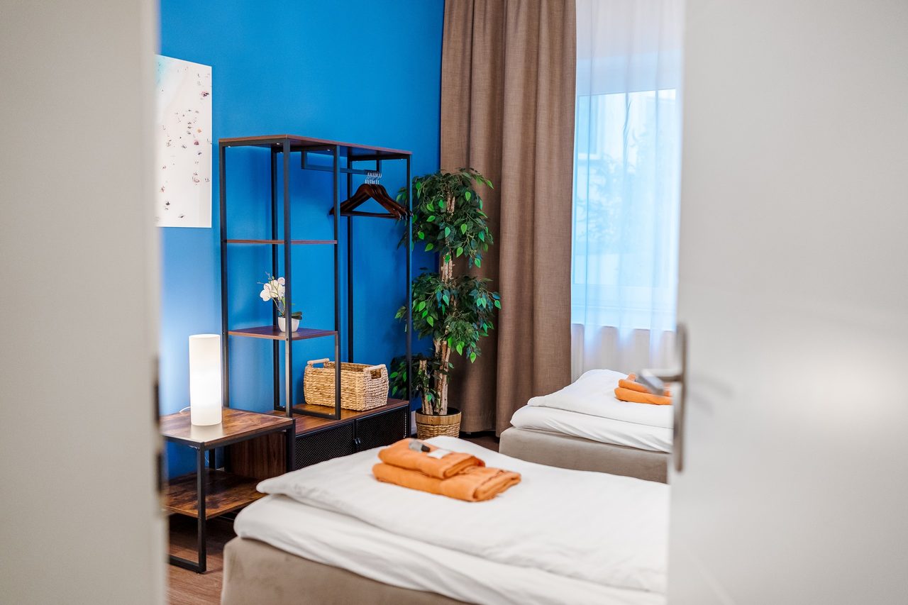Schlafzimmer mit zwei Betten, blauer Wand und Kleiderregal