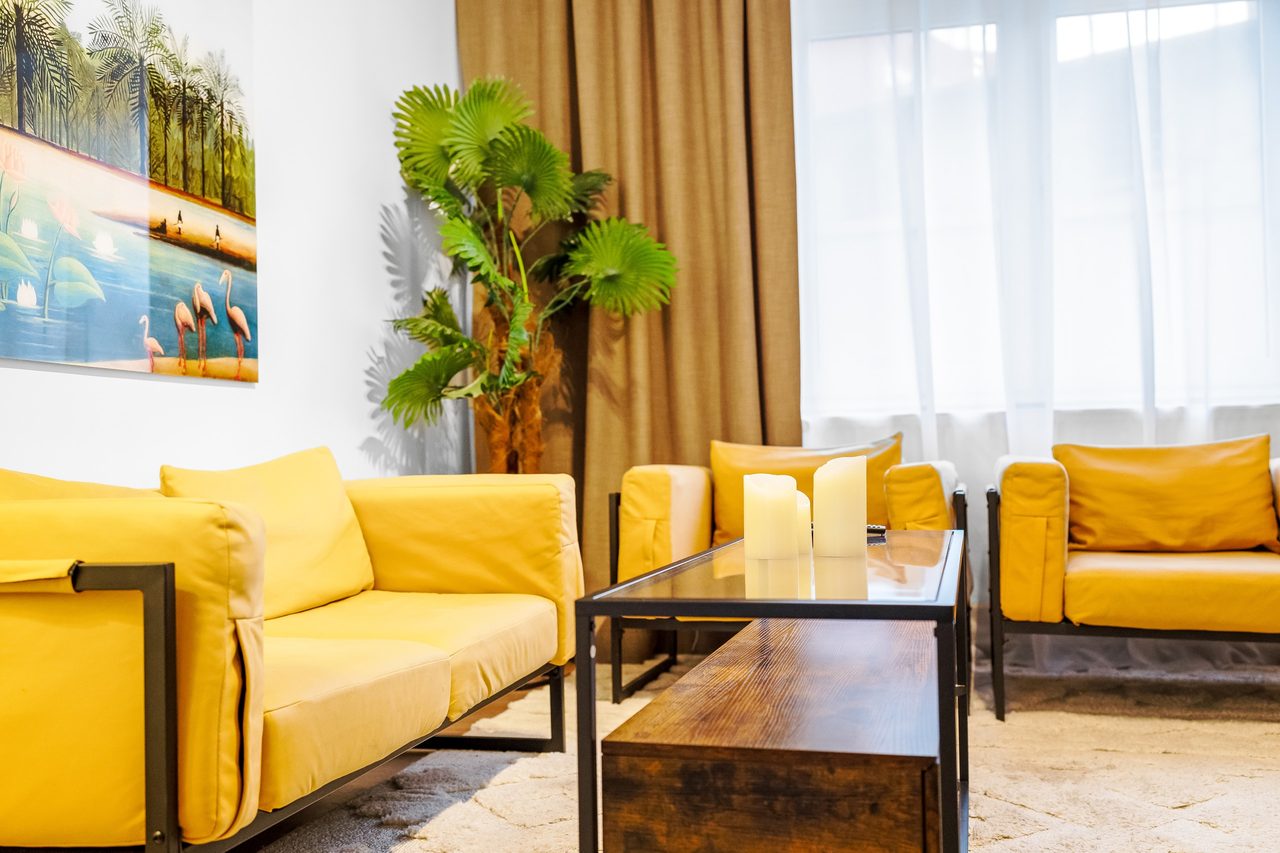 Wohnzimmer mit gelben Sofas, Couchtisch und großer Palme