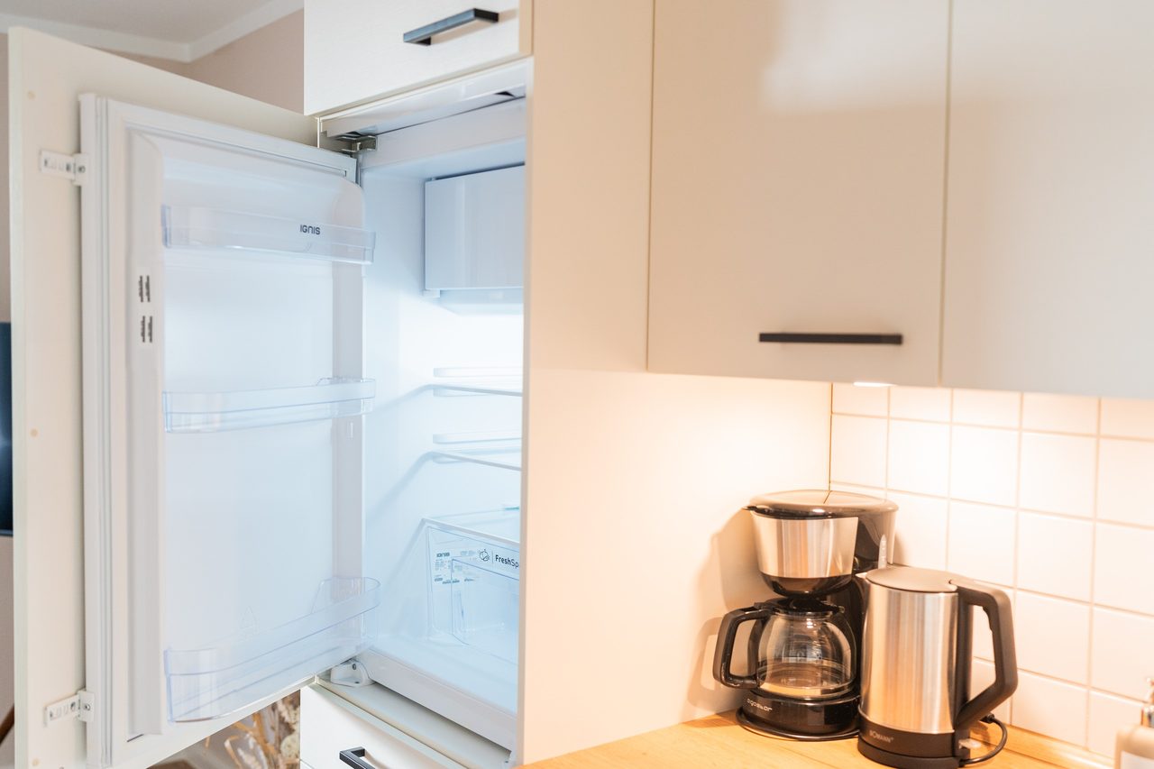 Offener Kühlschrank neben Kaffeemaschine und Wasserkocher