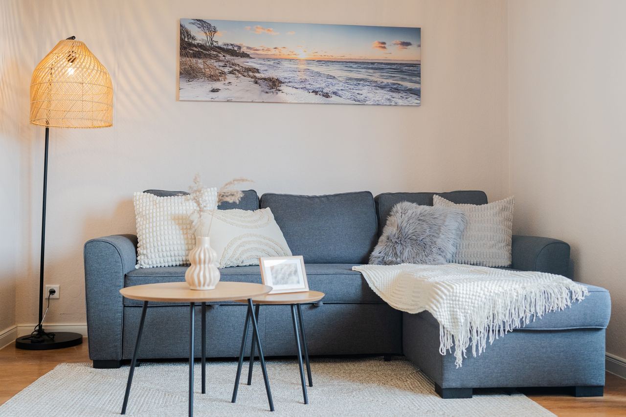 Wohnzimmer mit blauem Ecksofa, Beistelltischen, Stehlampe und Strandbild