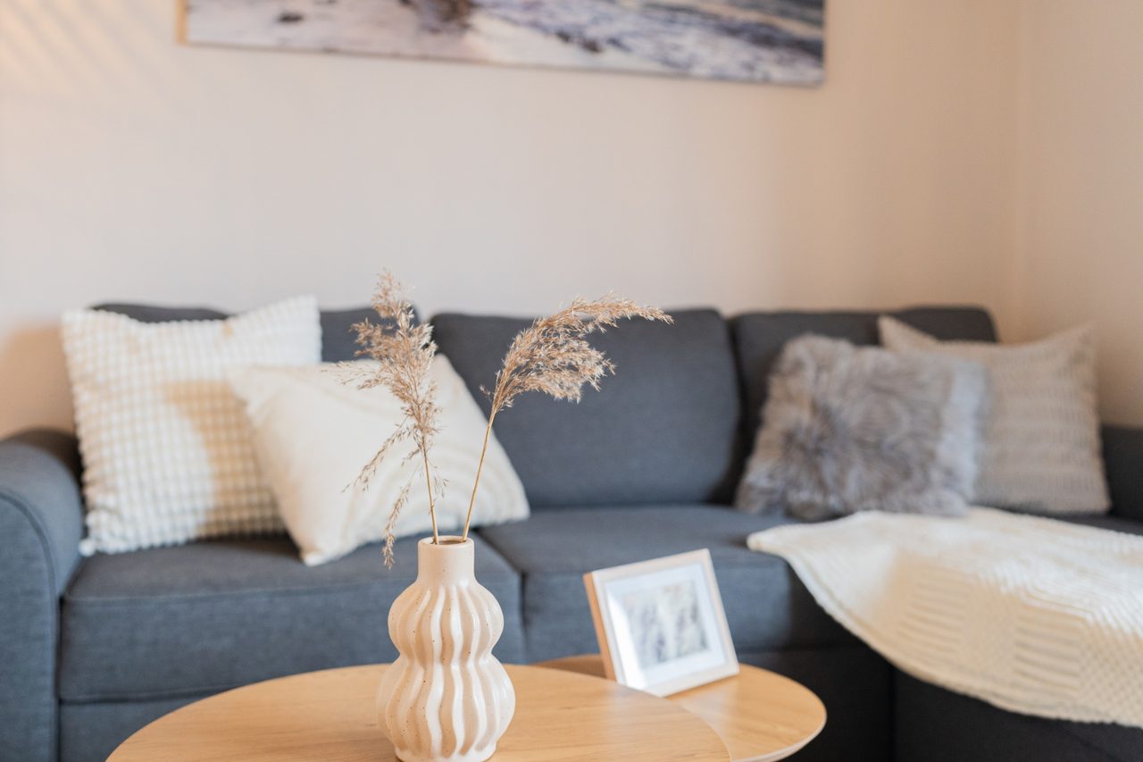 Blaues Sofa mit Kissen, Vase mit Trockengras und Bilderrahmen
