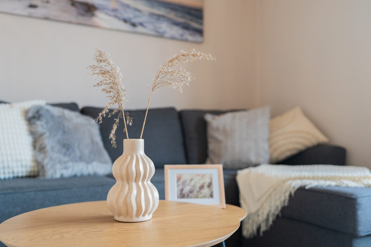 Vase mit Trockengras und Bilderrahmen auf Tisch vor blauem Sofa